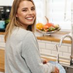Photo of woman smiling and looking at camera while washing dishes