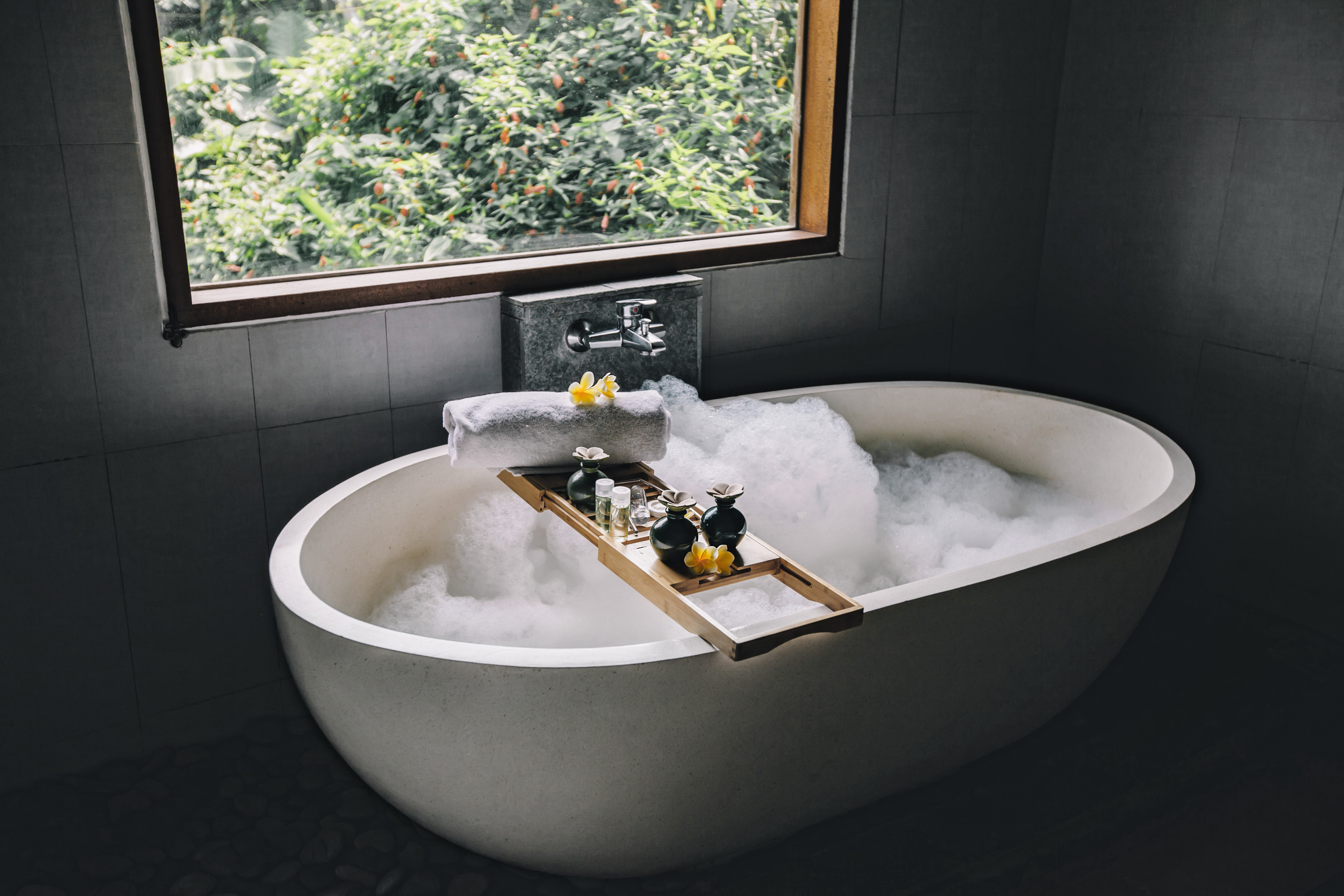 Bath with foam is filling with water, beauty products on bathtub