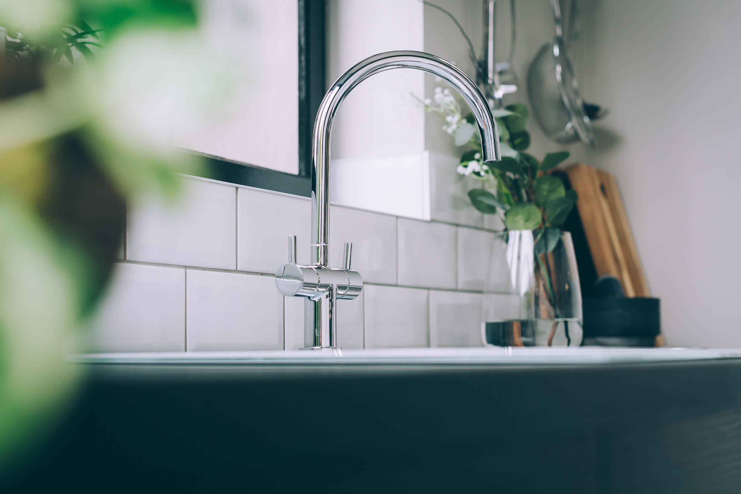 Shot of a modern sink with a white tiled wall in its back and some plants next to it