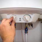 A hand adjusting the temperature settings of a water heater